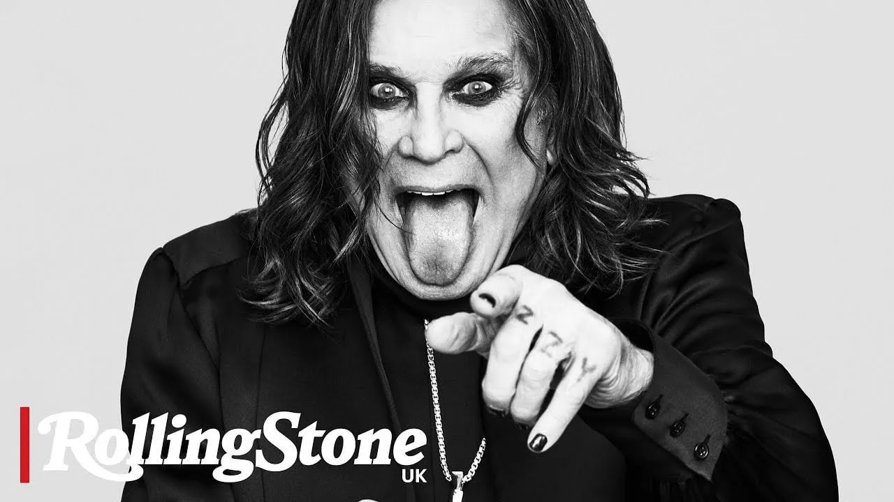 Ozzy Osbourne s rozcuchanými vlasy a výrazným make-upem, ukazuje na diváka.