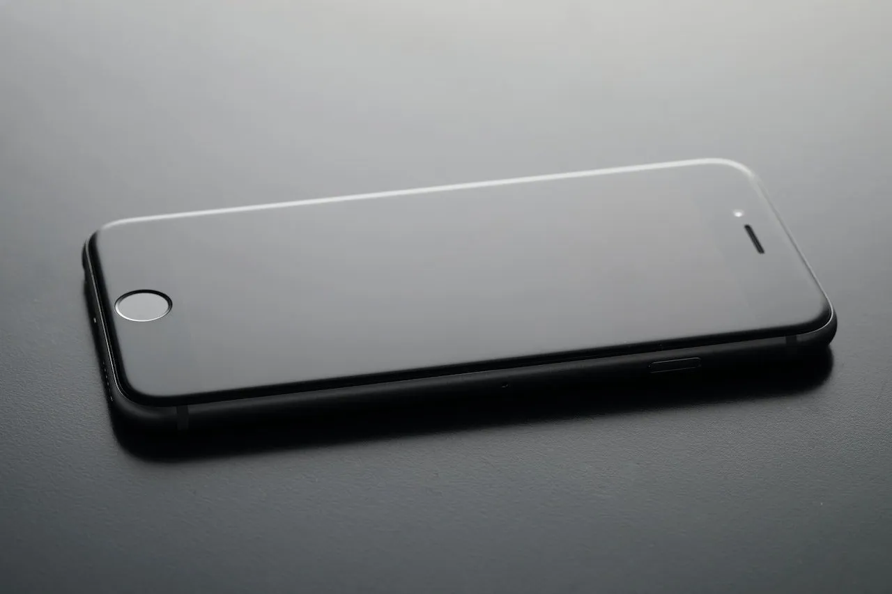 Černý chytrý telefon ležící na stole, obrazovka je vypnutá.